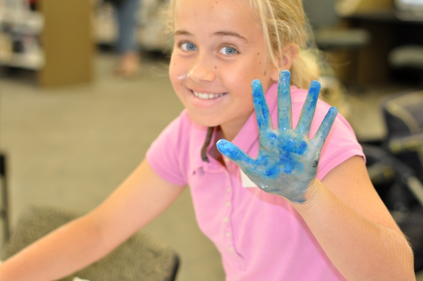 photo of smiling girl holding up a hand covered in blue paint