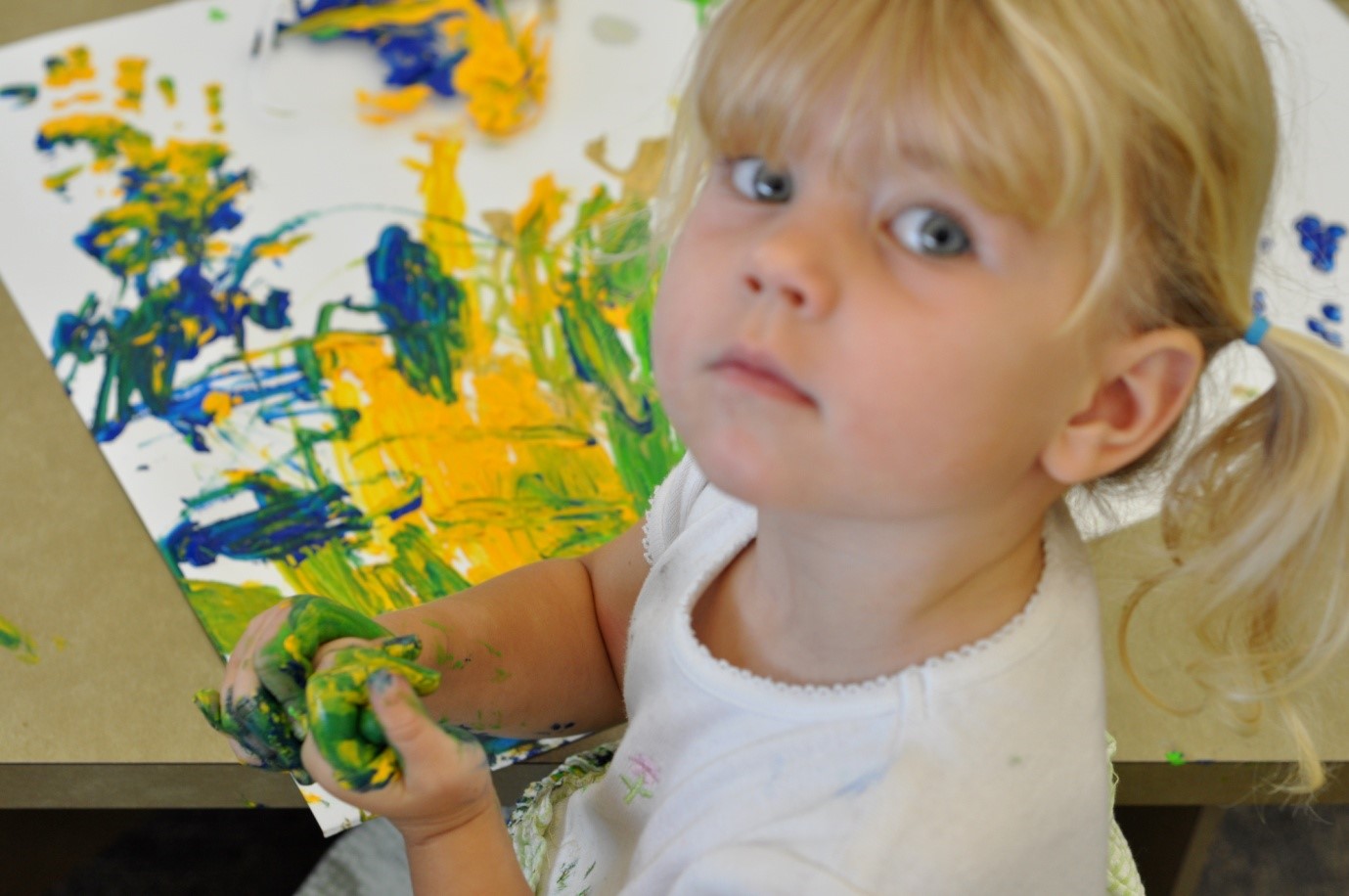 photo of young girl with paint colored hands next to her finger painted art piece